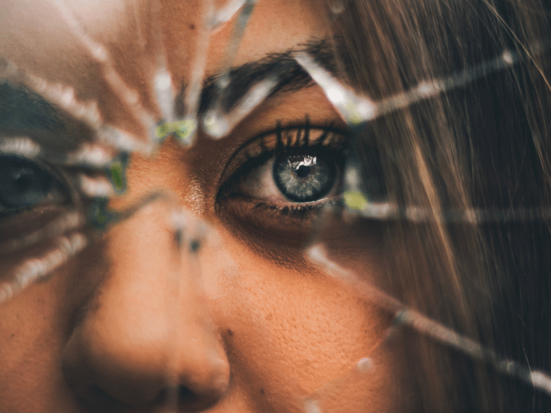 close up of woman's face behind a cracked and broken window